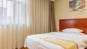 Una habitación de hotel con cama, cortinas, un cuadro en la pared y suelo de madera.