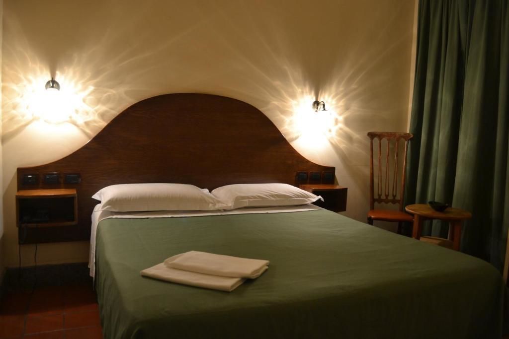 A hotel room with a large bed, two bedside tables, a wooden headboard, and two wall-mounted lights.