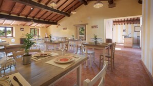 Un comedor amplio con mesas y sillas de madera, una cocina al fondo y un techo rústico con vigas a la vista.