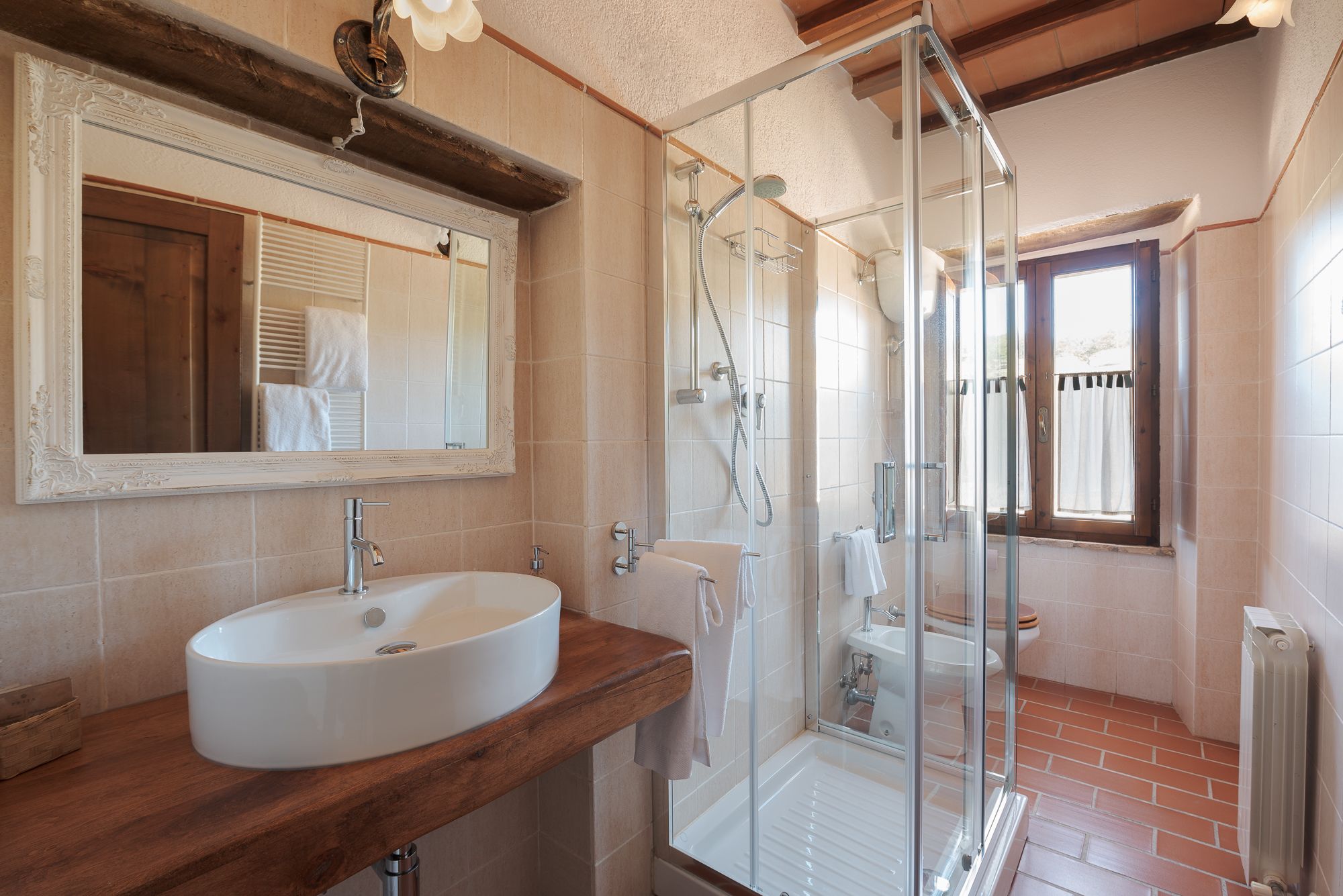 Un bagno con uno specchio grande, un lavandino, un box doccia e una finestra.