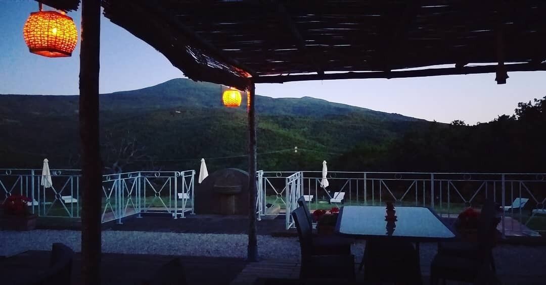 Una terraza al aire libre con vistas a una montaña, mesas, sillas y faroles colgantes.