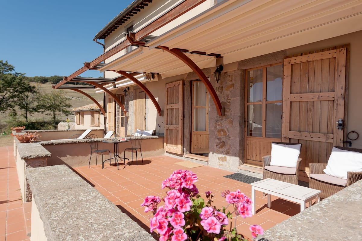 Un patio couvert avec des meubles d’extérieur, des murs en pierre et des volets en bois.