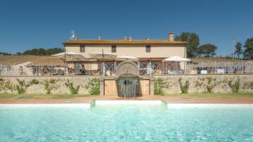 A hotel with a swimming pool, outdoor umbrellas, and a stone wall.