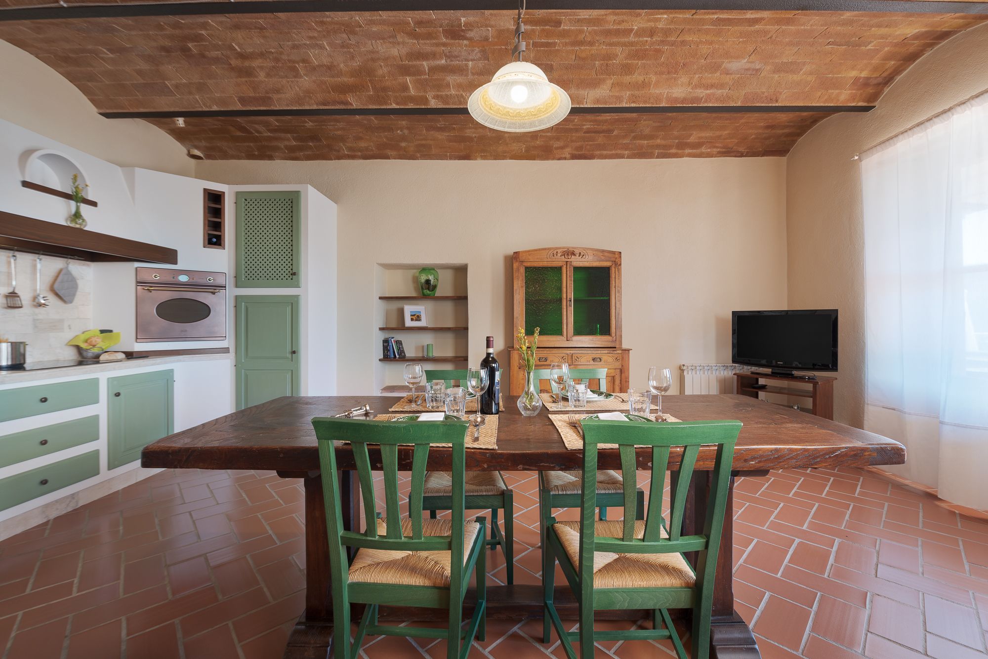 Un comedor con una mesa de madera, sillas verdes y una lámpara colgante.