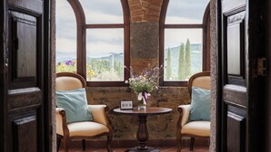 Una habitación con dos sillas, una mesa con un jarrón de flores y vistas a las colinas a través de amplias ventanas.