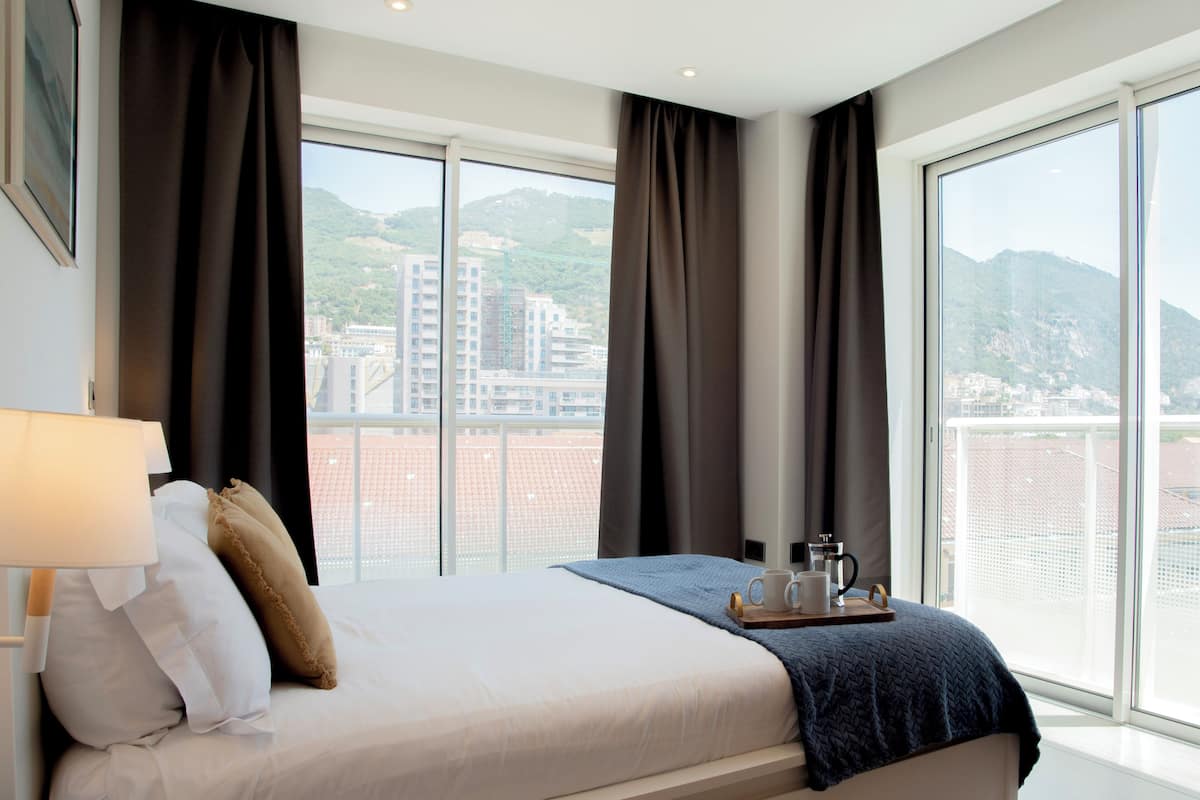 A hotel room with a large bed, a bedside table, a lamp, and a tray with two mugs.