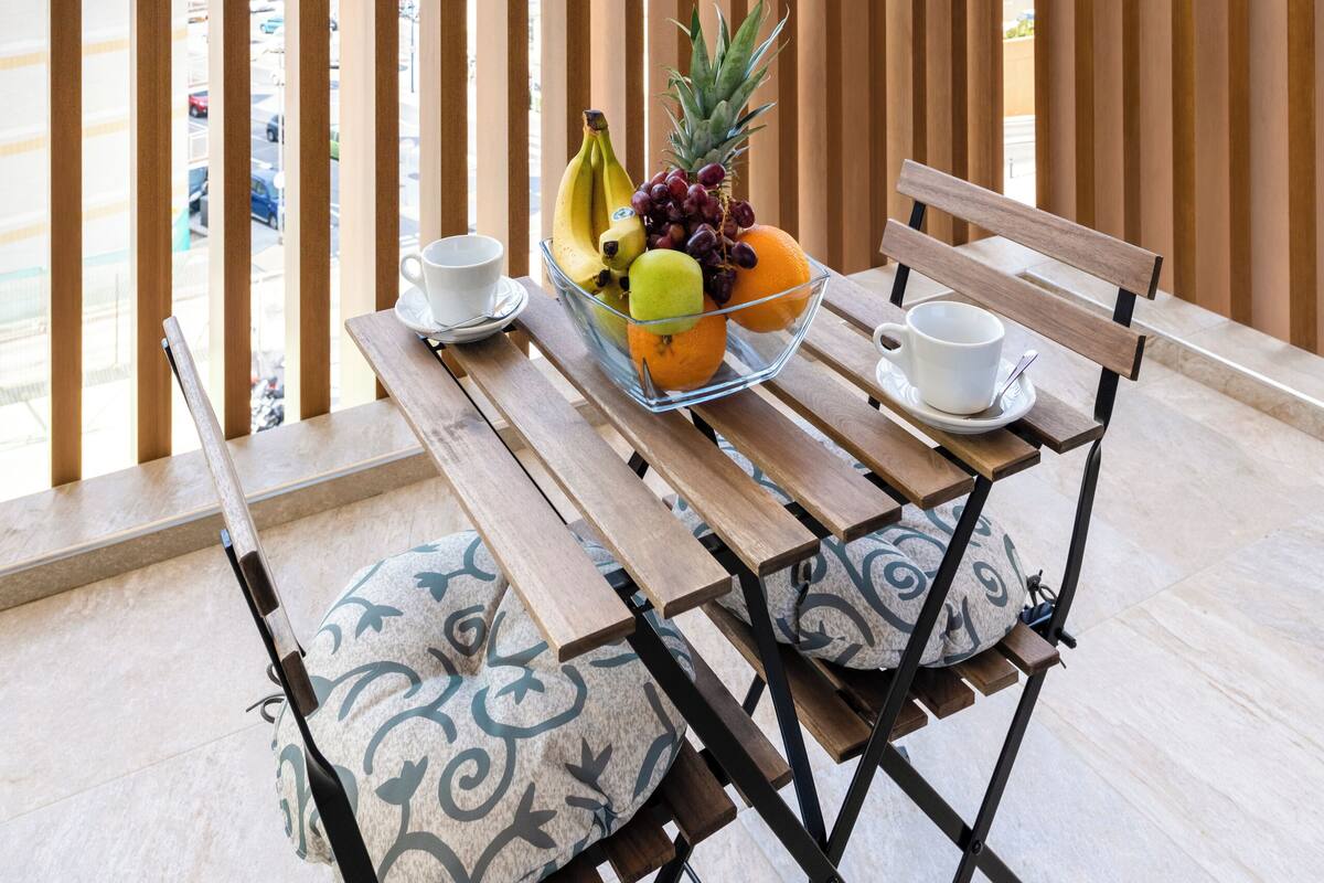 A balcony with a wooden table, two chairs, a bowl of fruit, and a cup.