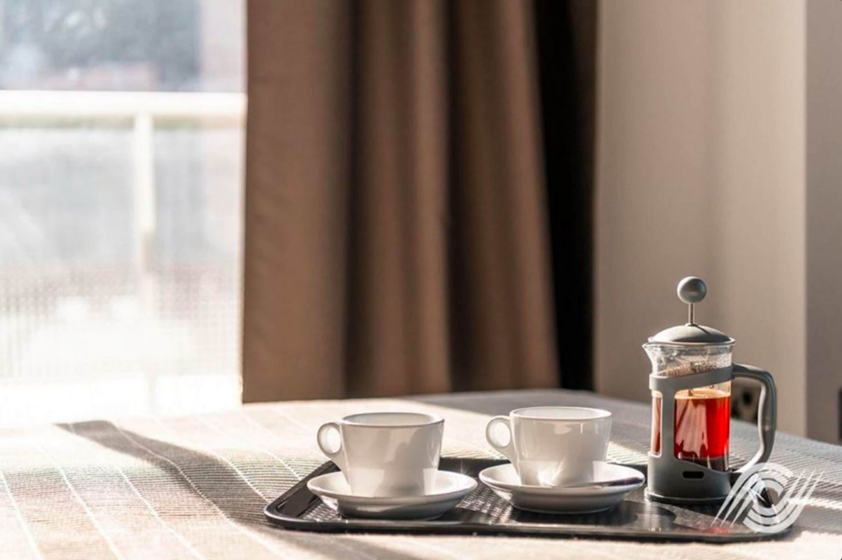 A breakfast setup with two white cups and a French press on a tray.
