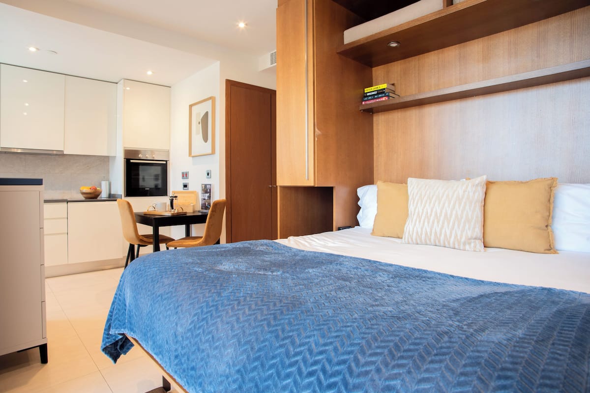 A modern hotel room with a bed, a desk, and a kitchenette.