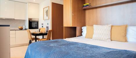 A modern hotel room with a bed, a desk, and a kitchenette.