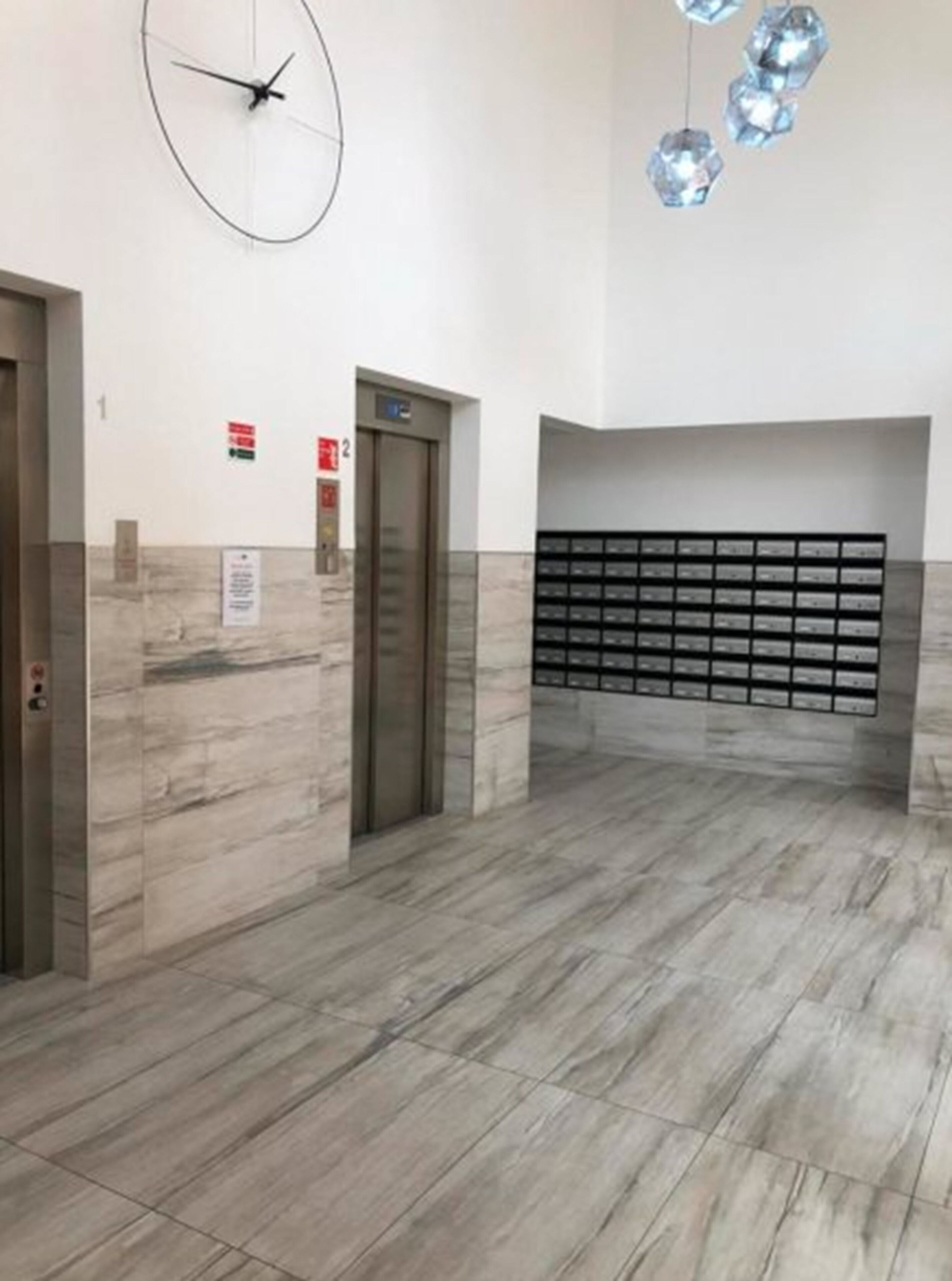 Un vestíbulo de ascensor moderno con suelo de mármol, un reloj en la pared y una lámpara decorativa.