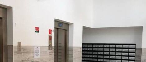 Un vestíbulo de ascensor moderno con suelo de mármol, un reloj en la pared y una lámpara decorativa.