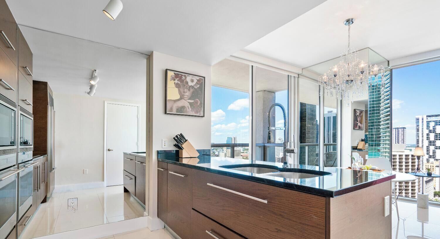 A modern kitchen with a large island, a chandelier, and a city view.