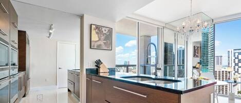 A modern kitchen with a large island, a chandelier, and a city view.