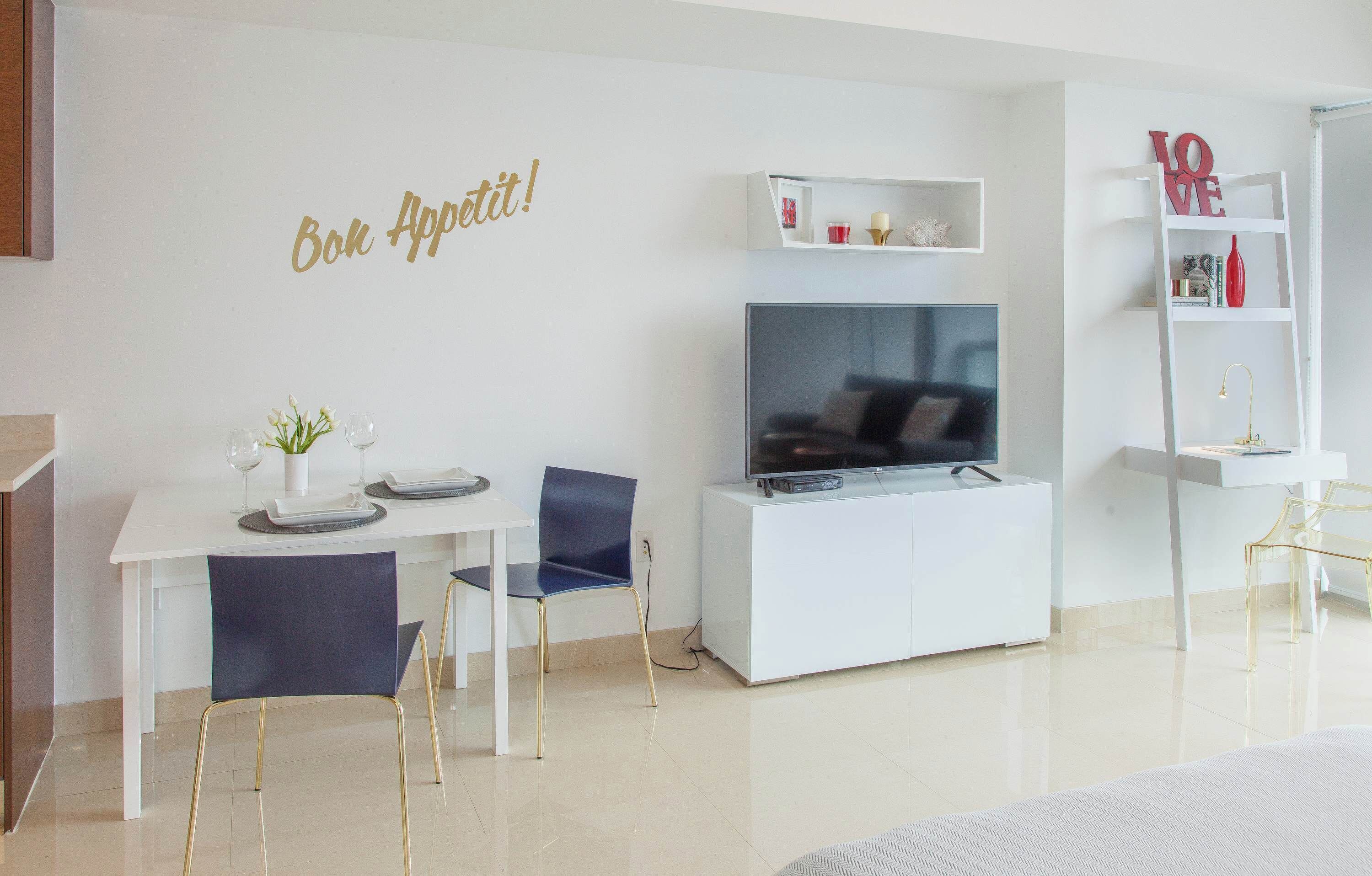 A modern living room with a dining area, a flat-screen TV, white furniture, and decorative items.