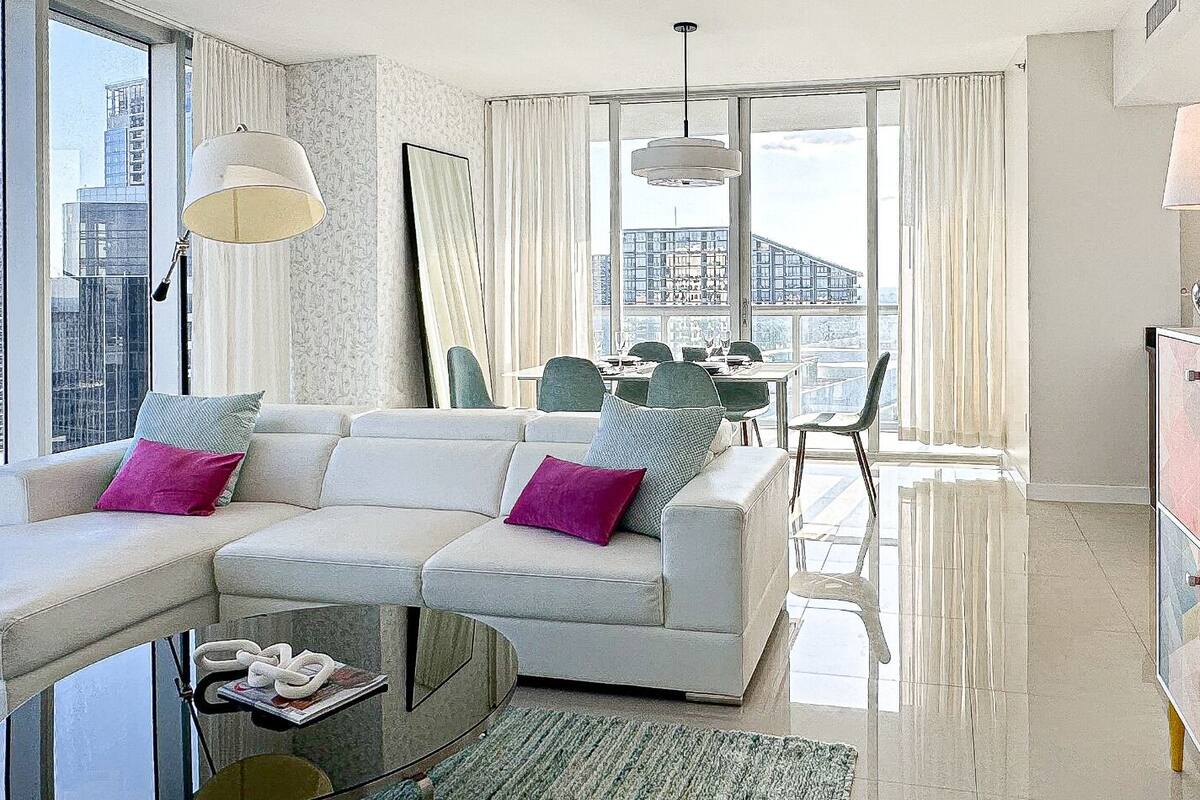 A modern living room with a sectional sofa, a glass coffee table, and a dining area with chairs and a table.
