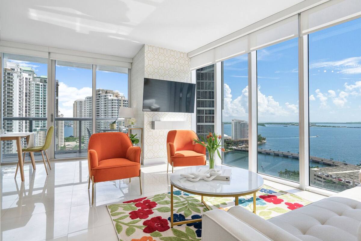 A modern living room with large windows, a flat-screen TV, and a view of the water.
