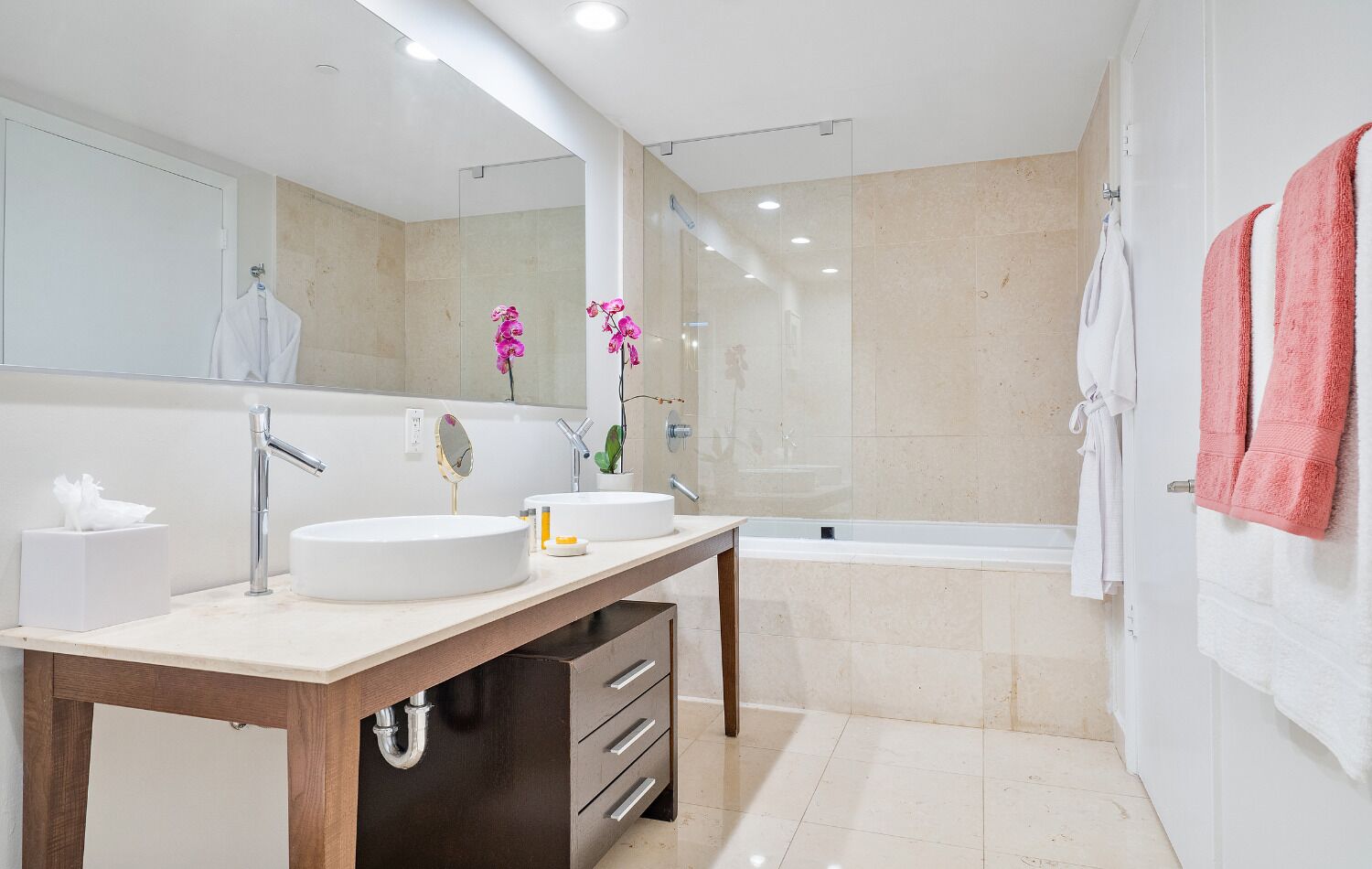 Uma casa de banho moderna com duas lavatórios, um espelho grande, toucador com gavetas, banheira e cabine de duche.