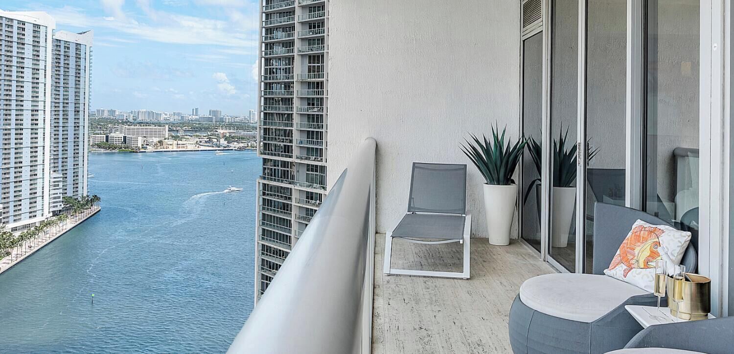 A balcony with a view of a body of water, a chair, a small table, and a potted plant.