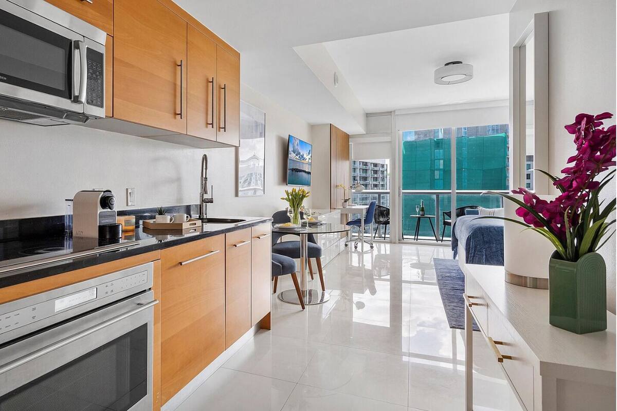 A modern kitchen with a Bosch microwave, wooden cabinets, and a dining area with a view of the city.