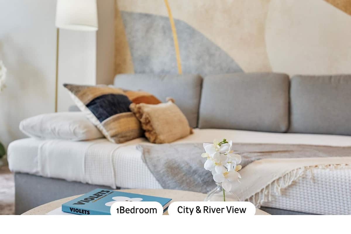 A bedroom with a sofa bed, a bedside table, and a vase with flowers.