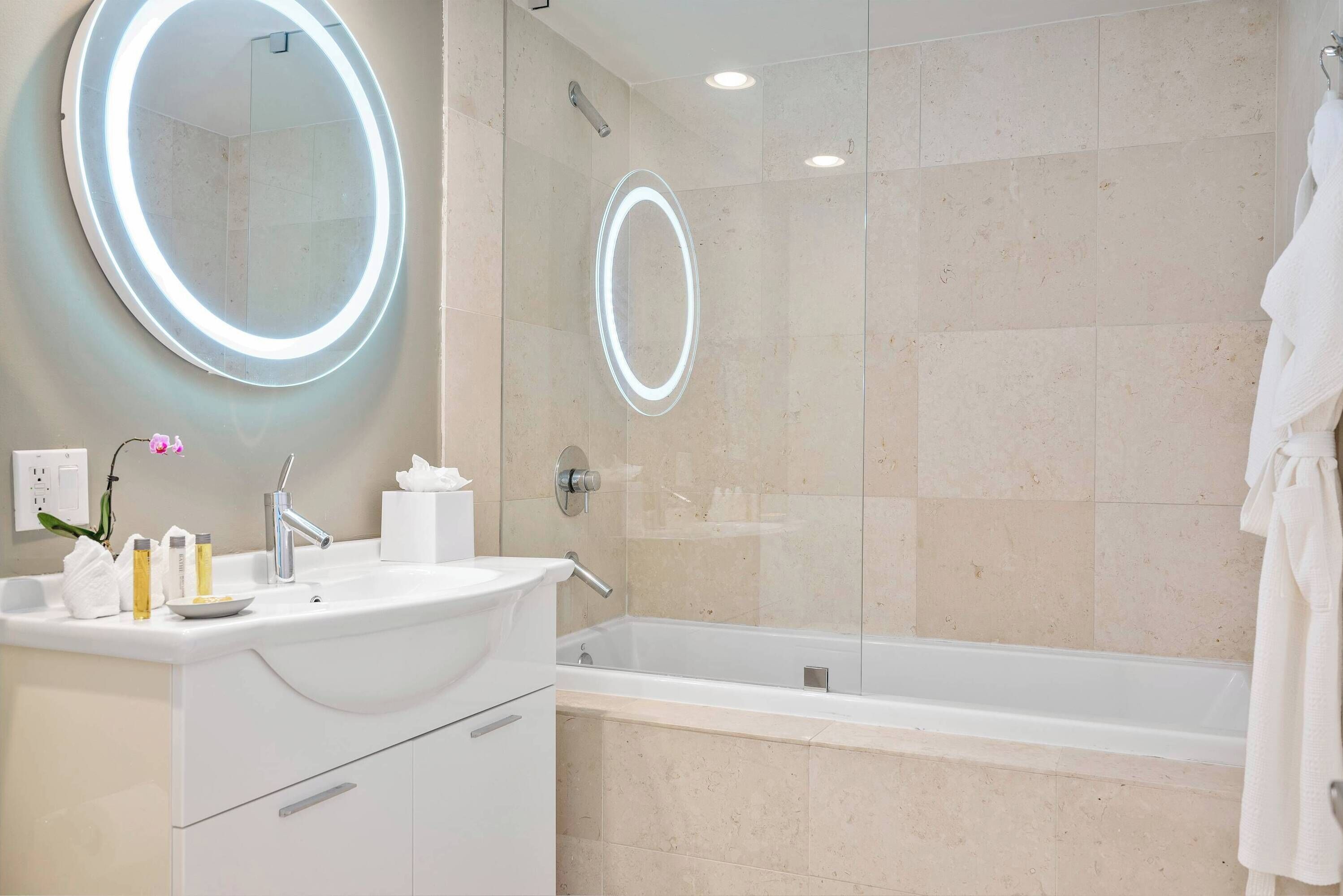 A modern bathroom with a round mirror, a bathtub, and a sink.