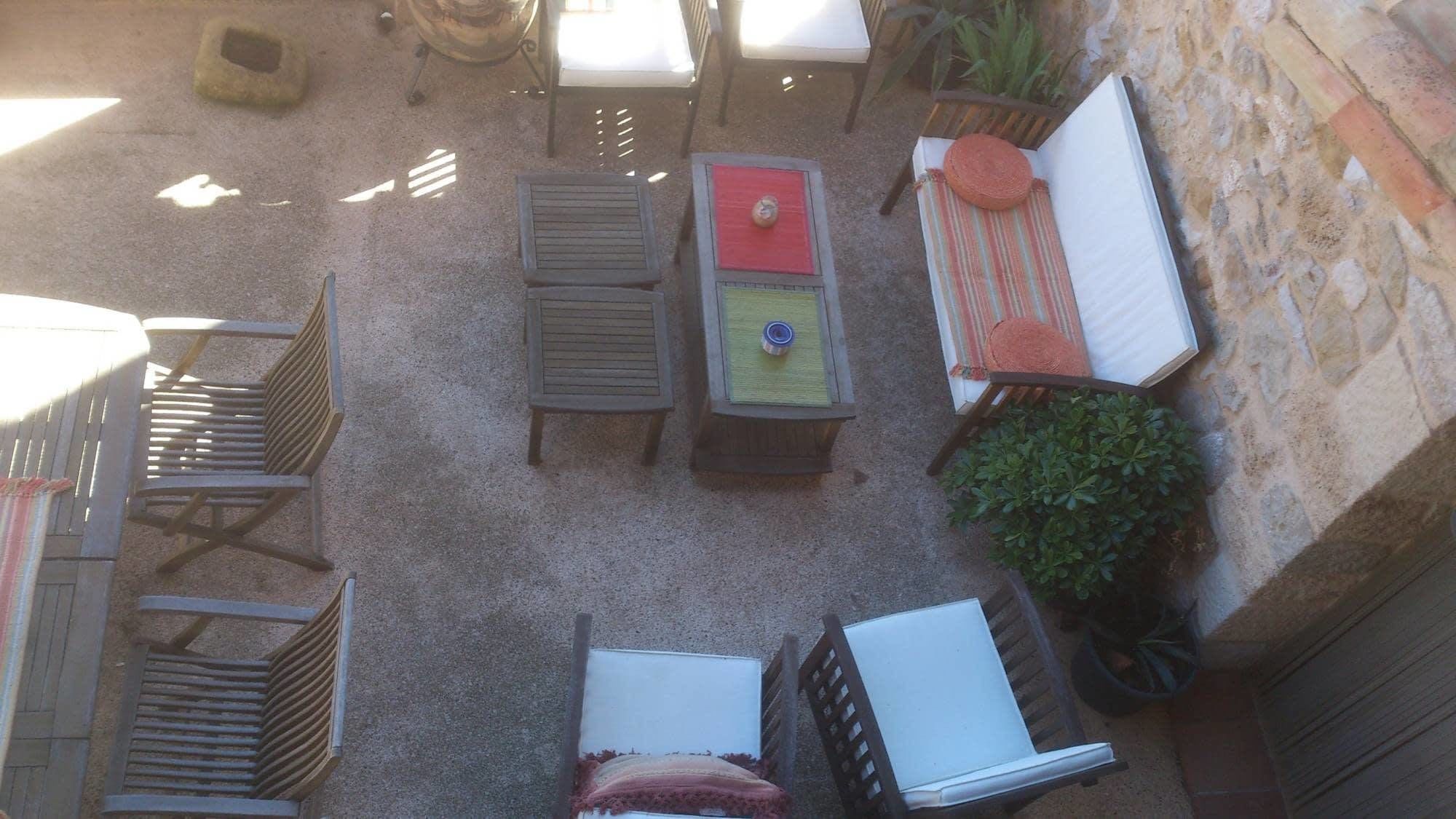 An outdoor patio area with a round table, two chairs, a small table with a red top, a striped cushion, and a potted plant.