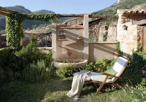 Un espacio de estar al aire libre de estilo rústico, con un muro de piedra, una silla de madera y una pequeña fuente.