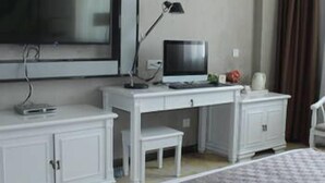A hotel room with a large flat-screen TV mounted on the wall, a desk with a computer, a small table, and a bed with a patterned bedspread. - The Straits Times Hotel (Fuzhou)