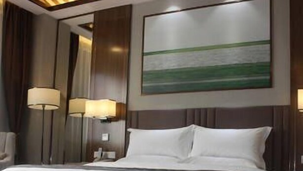 A hotel room with a large bed, two bedside lamps, a painting on the wall, and a striped carpet. - The Straits Times Hotel (Fuzhou)