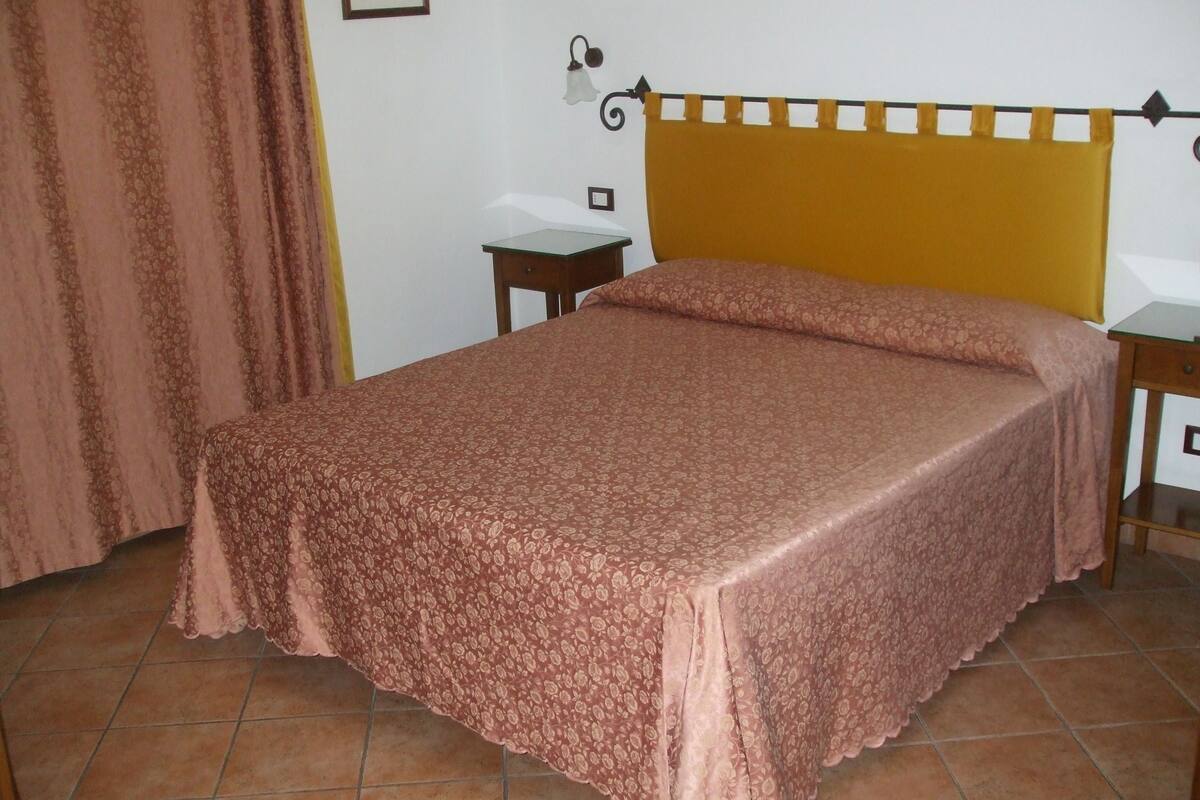 A room with a bed, a nightstand, a lamp, and a curtain.