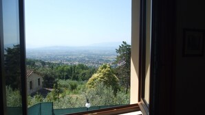 A window view of a cityscape with buildings and greenery. - Camere Ramaccia (Assisi)