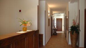 A hallway with a wooden reception desk, a digital clock, and a potted plant. - Camere Ramaccia (Assisi)