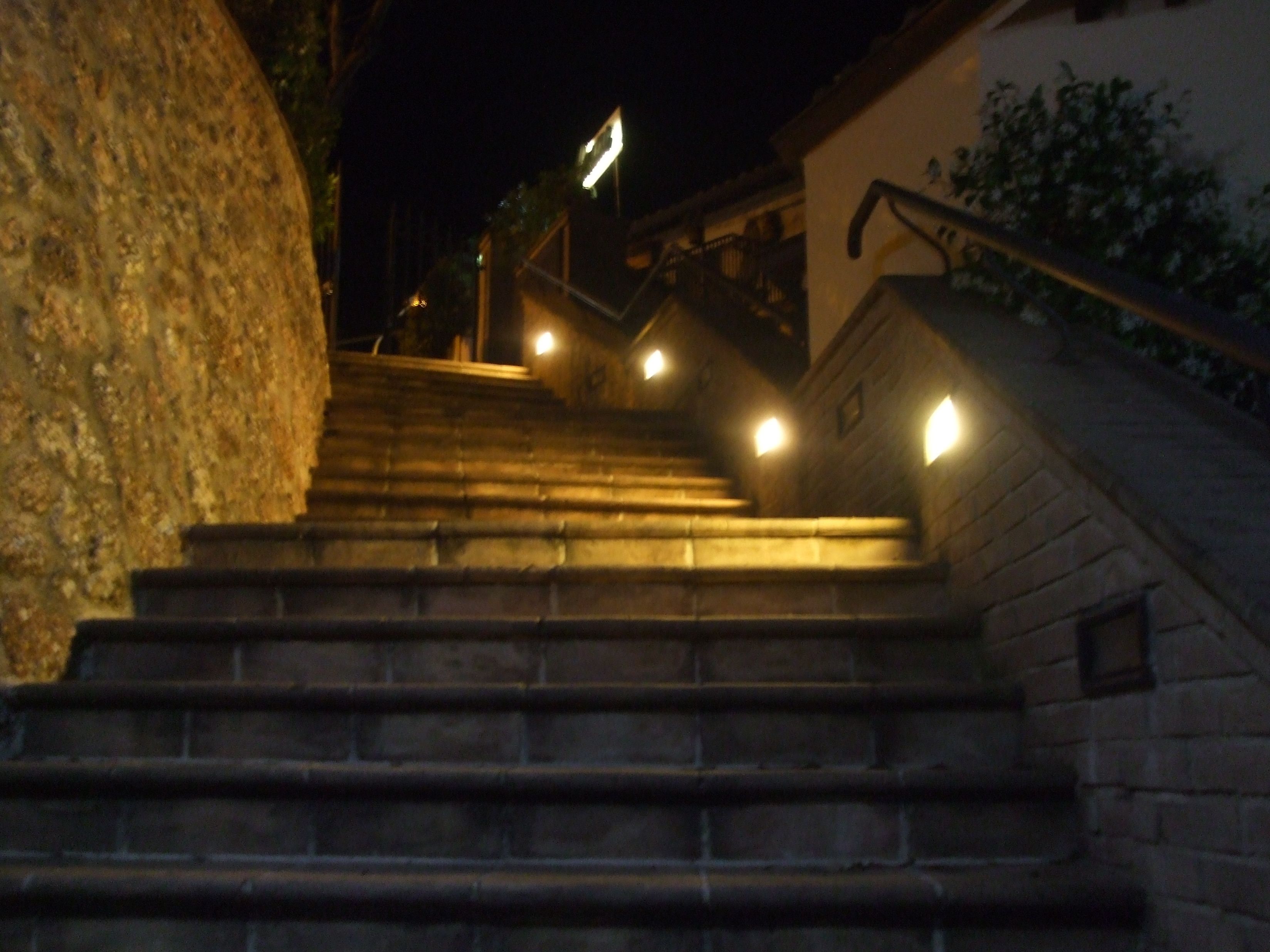 Una serie di gradini in pietra che portano a un edificio, con una ringhiera a destra.