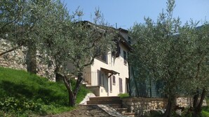 A two-story building with a stone facade, a staircase leading to the entrance, and surrounding olive trees. - Camere Ramaccia (Assisi)