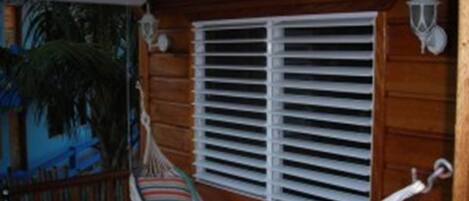 A wooden cabin with a hammock, a window with blinds, and a lantern.