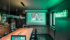 Une salle de conférence moderne, dotée d’une table en bois, d’un ordinateur portable et d’un écran de présentation affichant un message de bienvenue.