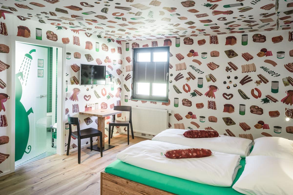 Ein Schlafzimmer mit einem hölzernen Bett, grüner Bettwäsche, einem Schreibtisch mit Stuhl und einer Wand mit Lebensmittellustrationen.