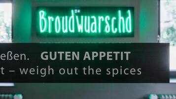 A neon sign with the text 'Broudwarschd' and a sign below stating 'GUTEN APPETIT - weigh out the spices'.