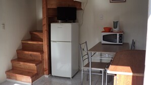 A compact kitchen with a refrigerator, microwave, and a dining area with a table and chairs. - Departamentos Arlenne II (Valdivia)