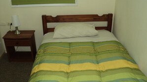 A single bed with a wooden headboard, a bedside table with a lamp, and a striped bedspread. - Departamentos Arlenne II (Valdivia)