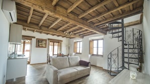 A spacious living area with a wooden ceiling, a sofa, a dining table, and a spiral staircase. - B&B Locanda Cistercense (Viterbo)