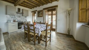A dining area with a wooden table and chairs, a kitchen in the background, and a wooden ceiling. - B&B Locanda Cistercense (Viterbo)