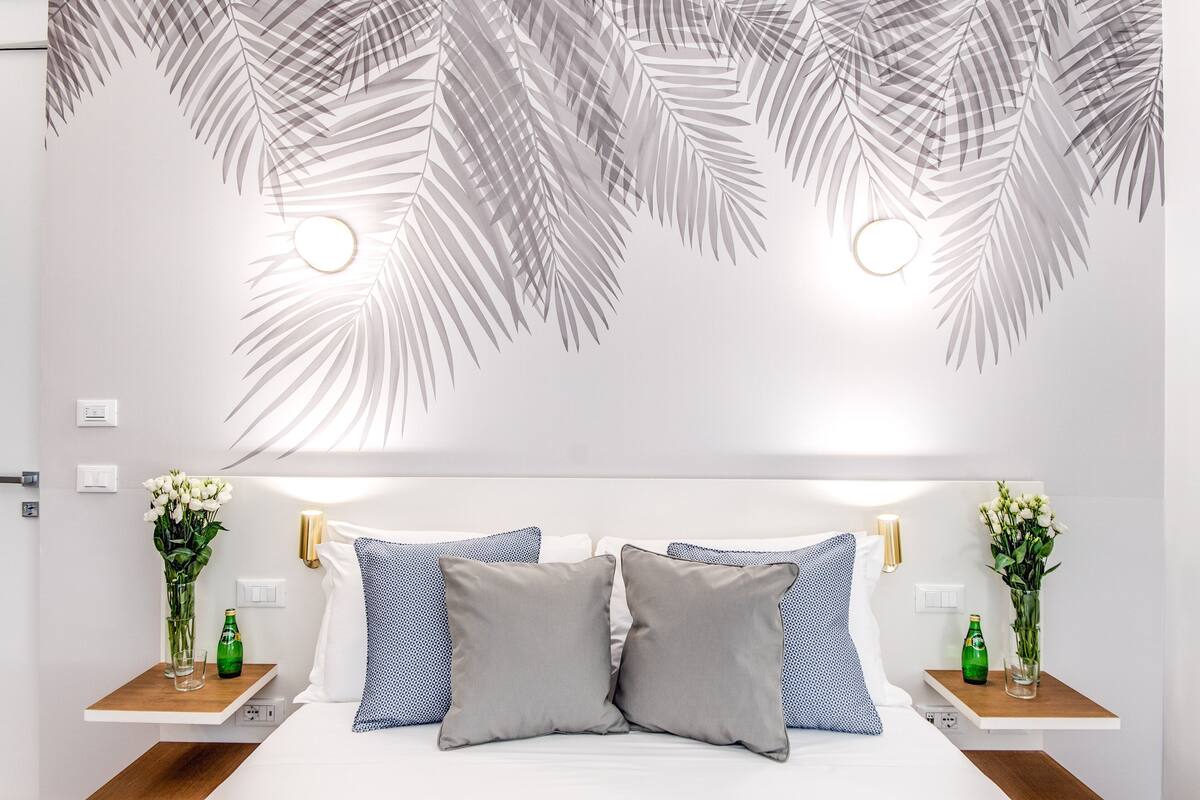 A bedroom with a bed, two nightstands, and wall-mounted lighting.