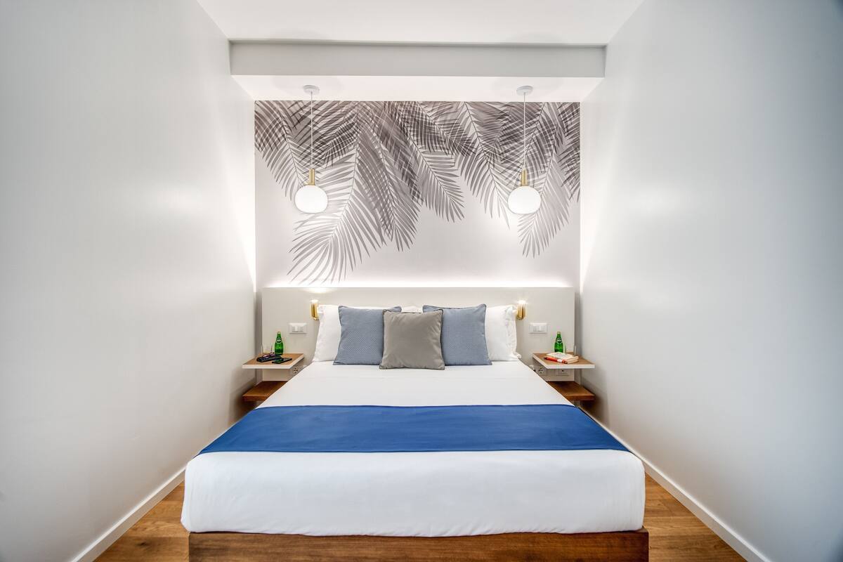 A modern hotel room with a large bed, white walls, and a decorative leaf pattern on the ceiling.