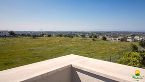 A balcony with a clear view of a distant cityscape, a grassy field, and a few buildings in the background. - Marilu B&B (Matino)