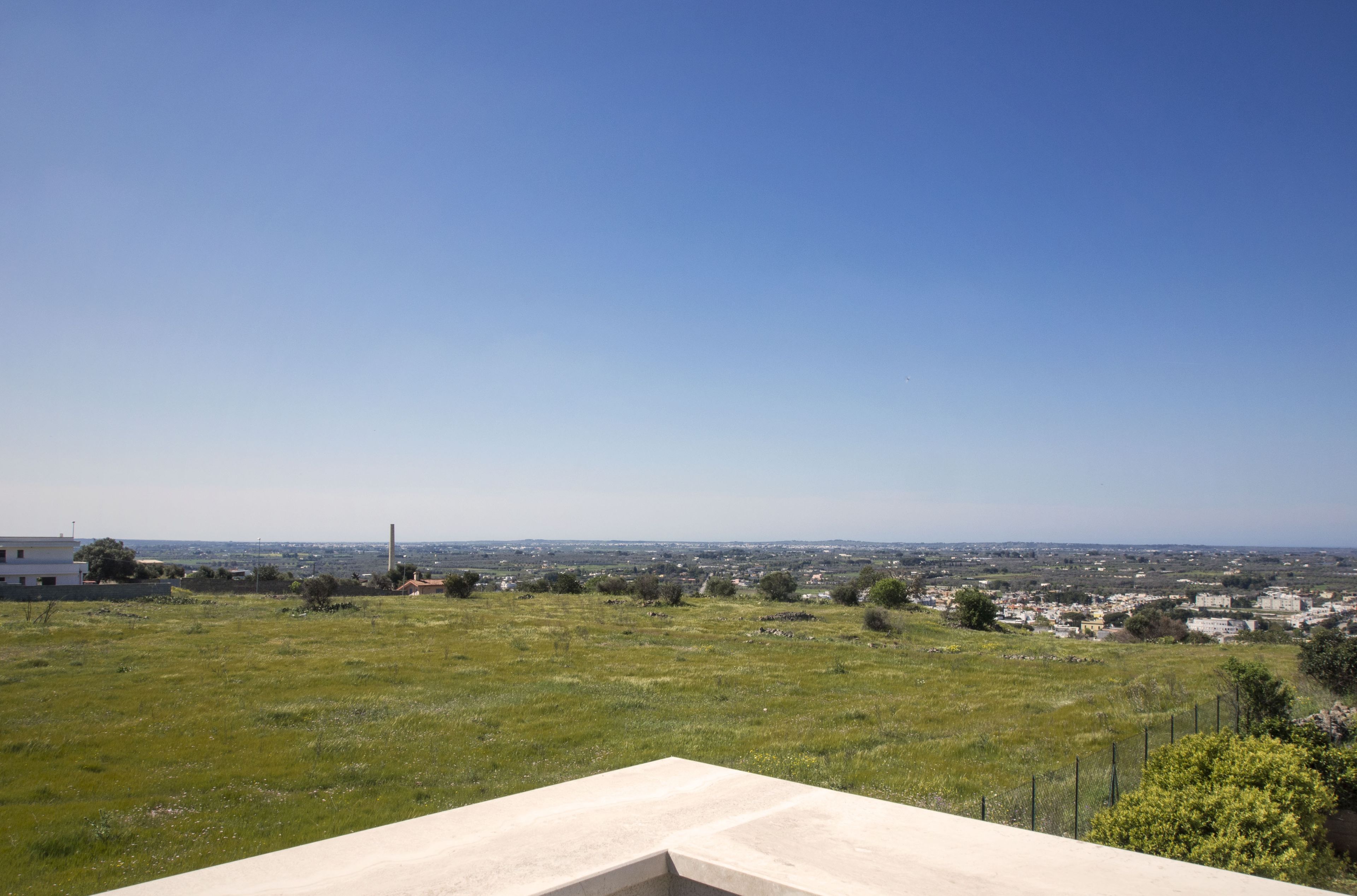 A view from a balcony overlooking a grassy field with a distant cityscape.