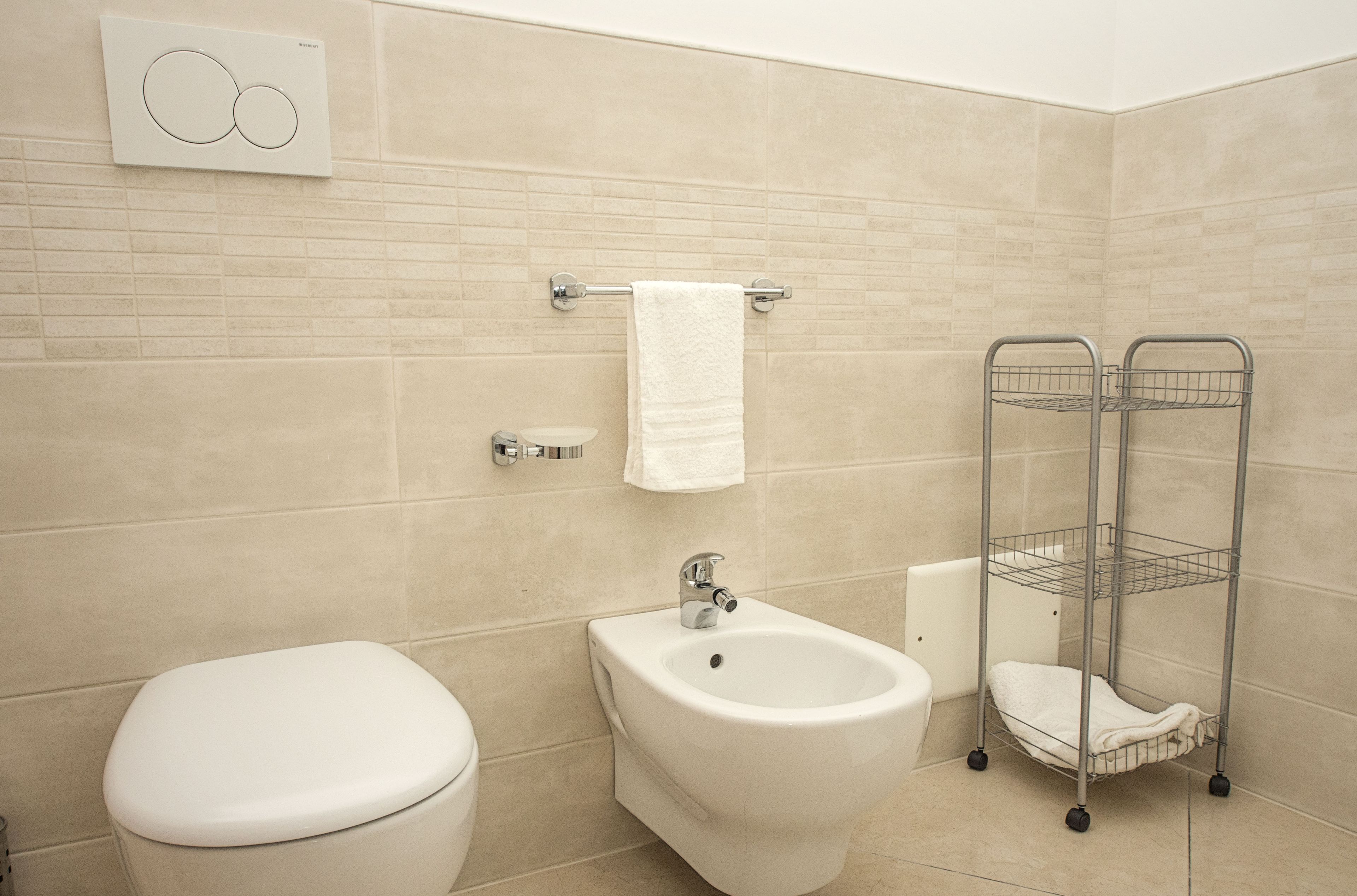 Et badeværelse med toilet, bidet og et metalhåndklædetørrestativ.