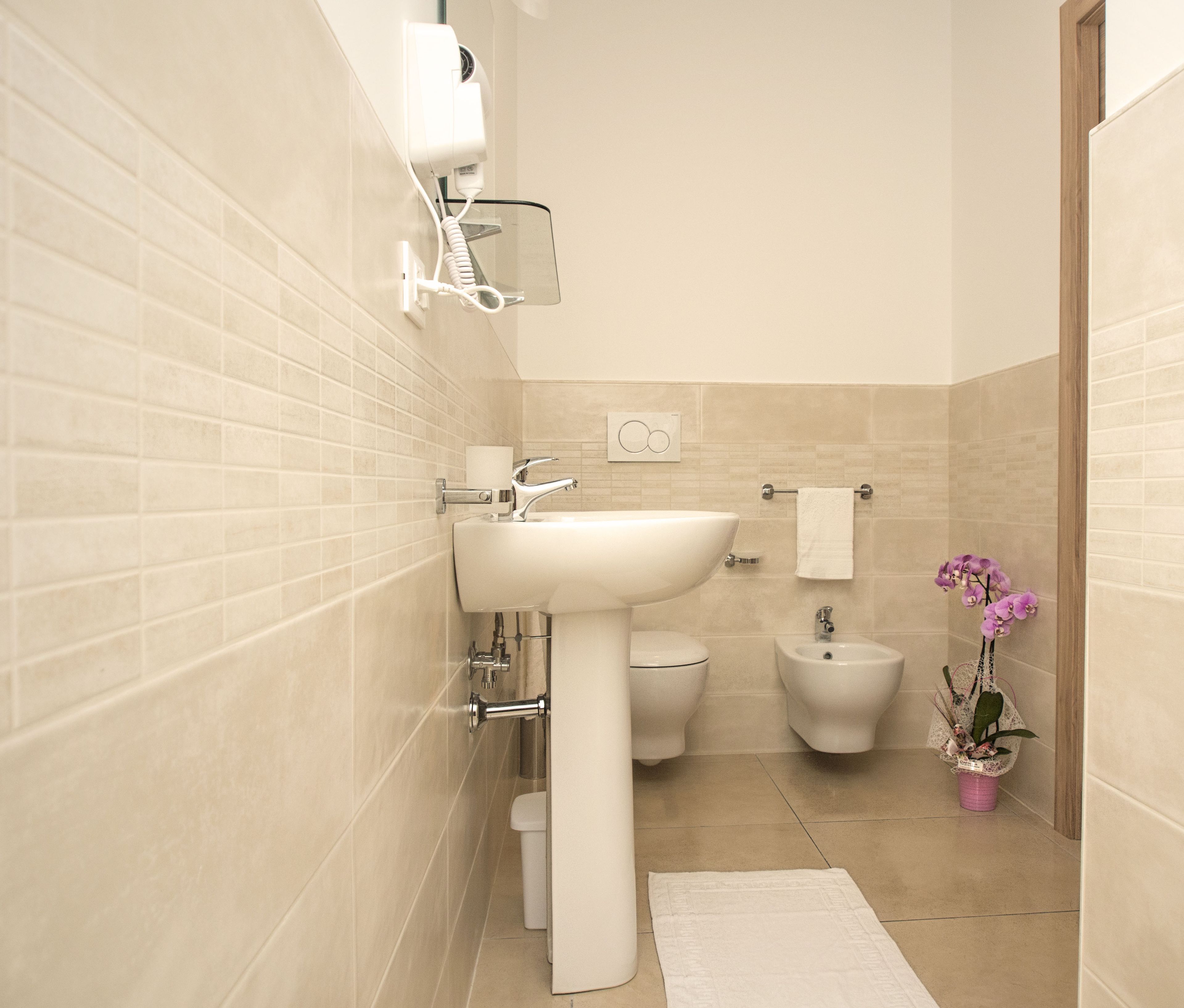 Un baño moderno con un lavamanos blanco, inodoro, bidé y un pequeño cubo de basura.