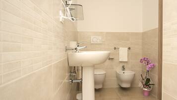 Un baño moderno con un lavamanos blanco, inodoro, bidé y un pequeño cubo de basura.